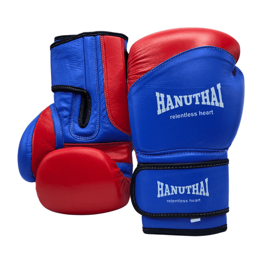 A pair of Hanuthai Muay Thai boxing gloves in blue and red with the text "hanuthai relentless heart" printed on them, positioned against a green background.