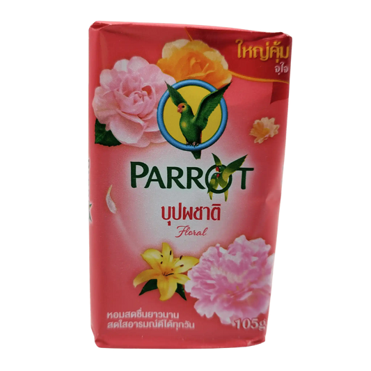 Parrot Botanicals' Parrot Herbal Soap Floral Bouquet (105g) packaging showcases vibrant pink and yellow floral images with the iconic green parrot logo. Perfect for skincare routines, it features Thai text, emphasizing its distinct floral scents.